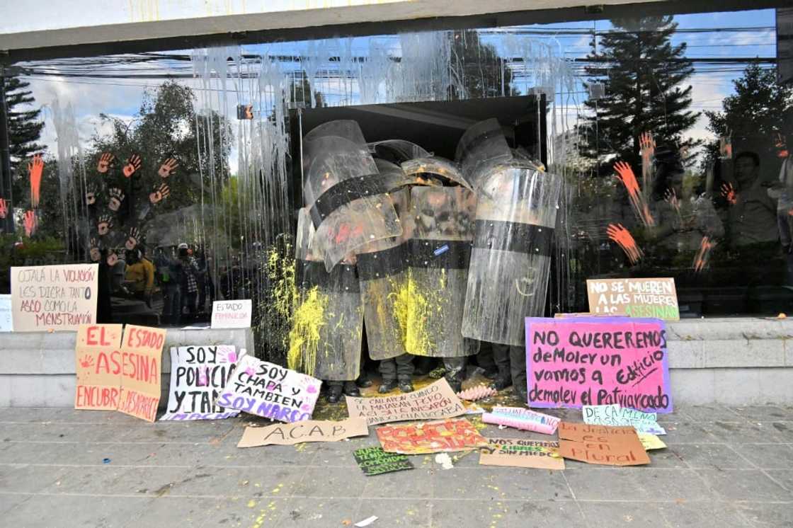 Officers in riot gear stand guard as a group of women protest in front of Ecuador's police headquarters