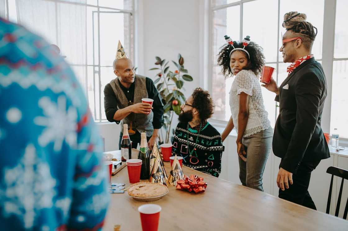 A group of people stand around a table celebrating with drinks and food. A group of people stand around a table celebrating with drinks and food.