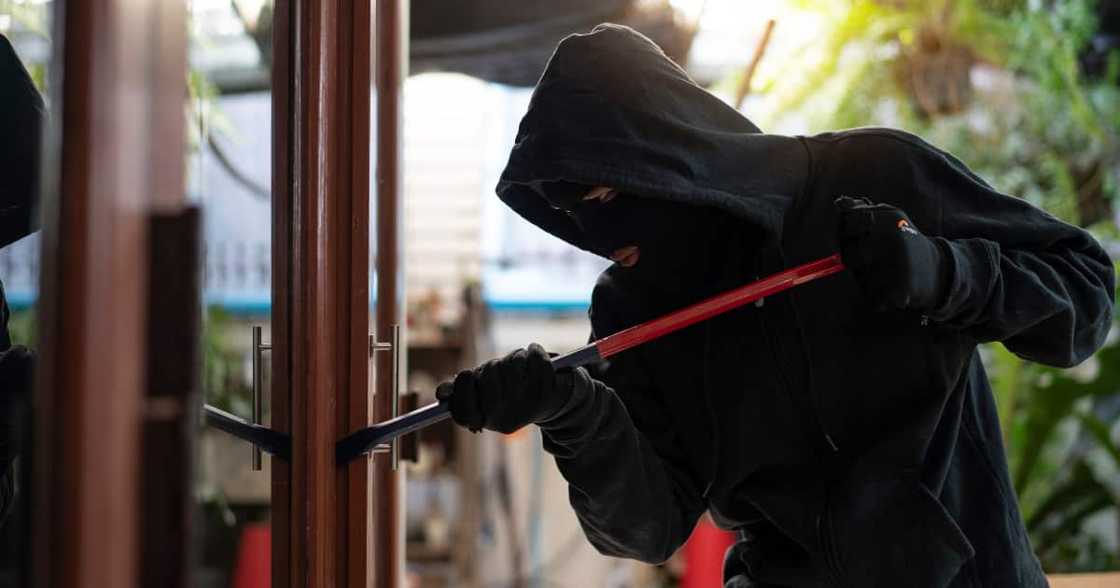 Burglar wearing black clothes and leather coat breaking in a house