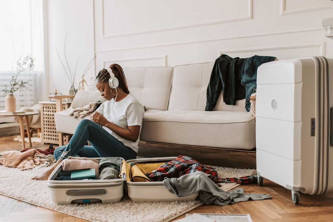 A woman sits on the floor with a messy open suitcase. A woman sits on the floor with a messy open suitcase.