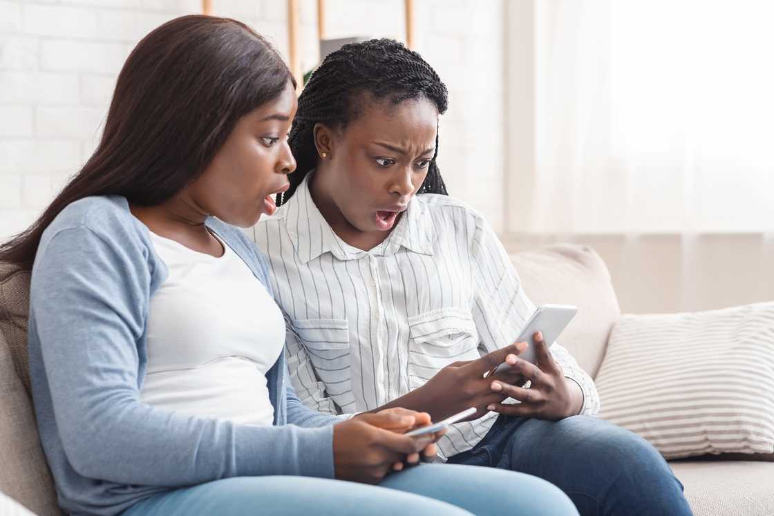 Two people on a couch react with surprise while looking at a phone.