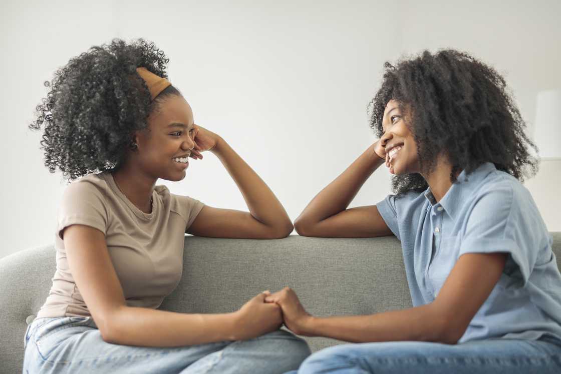 Two affectionate girlfriends laughing while sitting on sofa at home