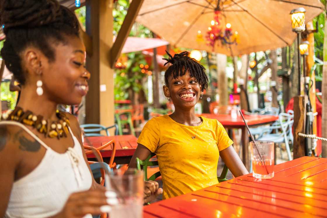 Two people sit at a red outdoor café table, smiling and enjoying drinks under decorative lights.