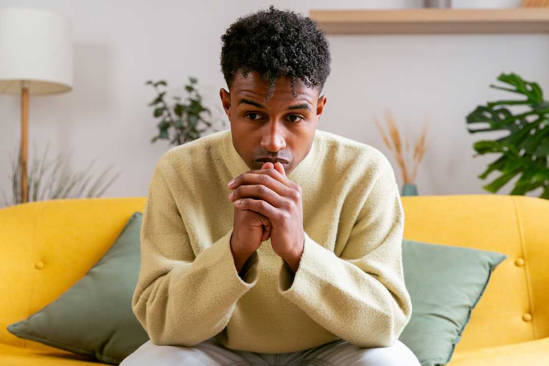 Young adult man sitting on sofa at home feeling stressed Young adult man sitting on sofa at home feeling stressed