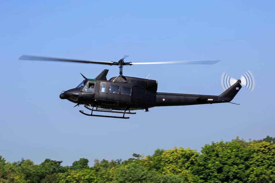 A black helicopter flying over green trees A black helicopter flying over green trees