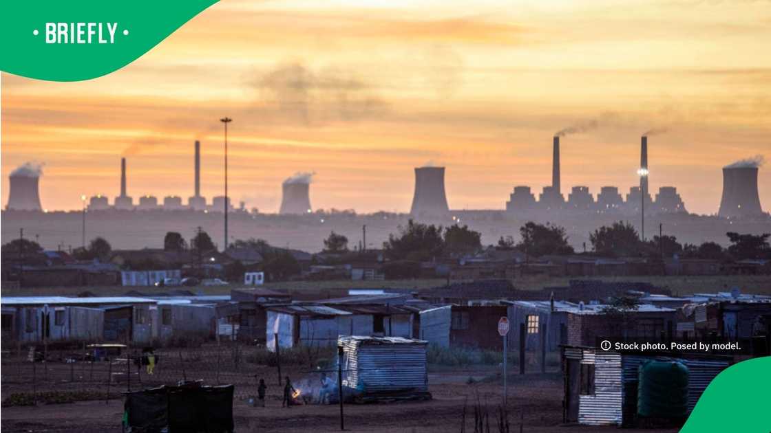 A family lit a small fire for cooking outside their informal home in Thubelihle, Mpumalanga, against a distant backdrop of the Eskom-run Kriel and Matla power stations at sunset