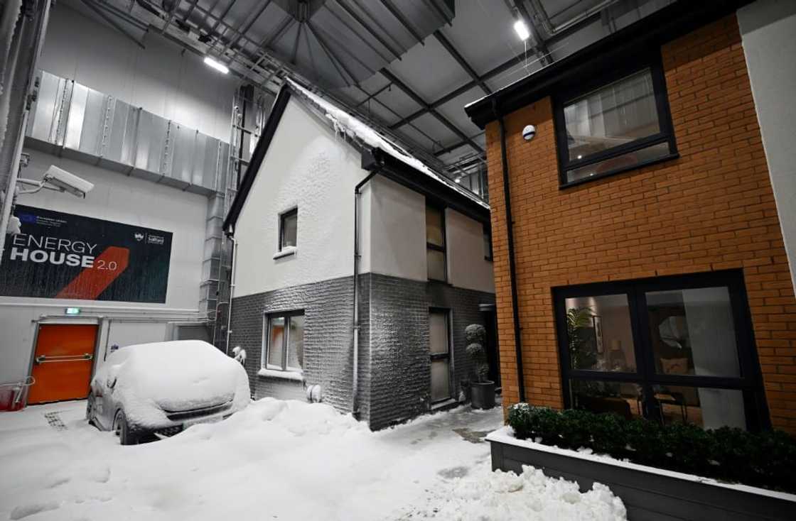 Simulated snow covers a car and the walls of one of two houses built in a lab to develop future heating solutions that will use less energy and help meet climate goals