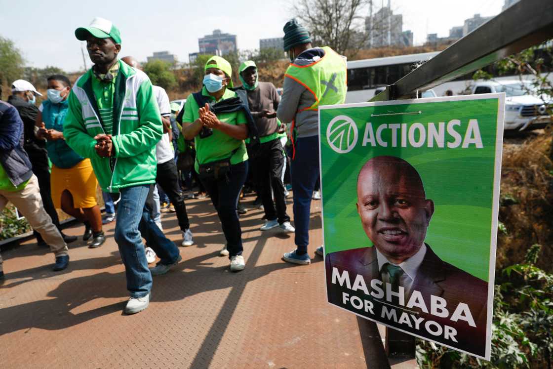 Action South Africa supporters walk past a poster showing the face of their leader Herman Mashaba during the partys manifesto launch for the upcoming local government elections at the Old Park Station in Johannesburg, on September 22, 2021 Action South Africa supporters walk past a poster showing the face of their leader Herman Mashaba during the partys manifesto launch for the upcoming local government elections at the Old Park Station in Johannesburg, on September 22, 2021