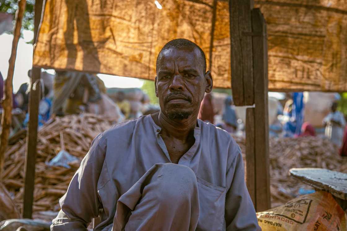 A middle-aged man sitting in a busy outdoor market stall. A middle-aged man sitting in a busy outdoor market stall.