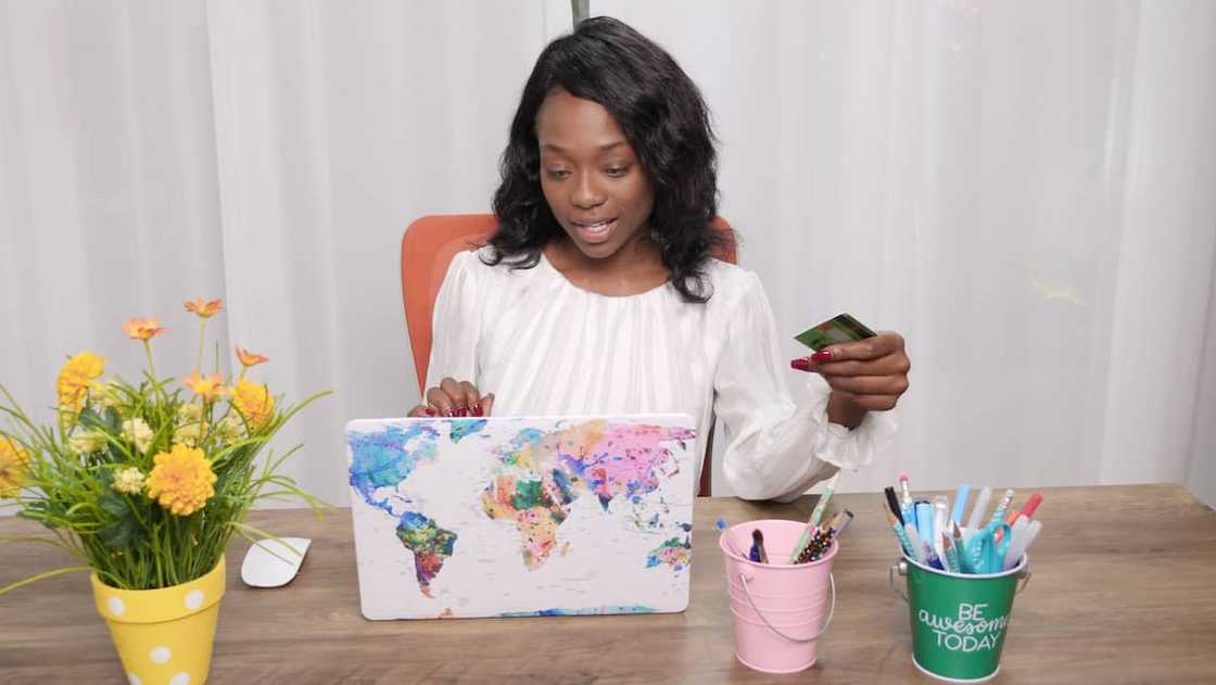 A woman in a white top using the laptop while holding a bank card