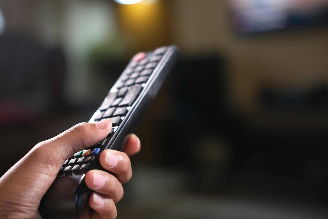 A black hand holds a remote control for the television