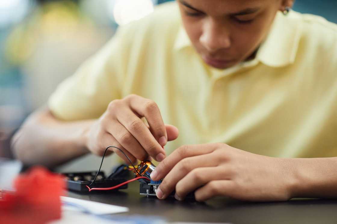 A teenager assembles electronic components at a table. A teenager assembles electronic components at a table.