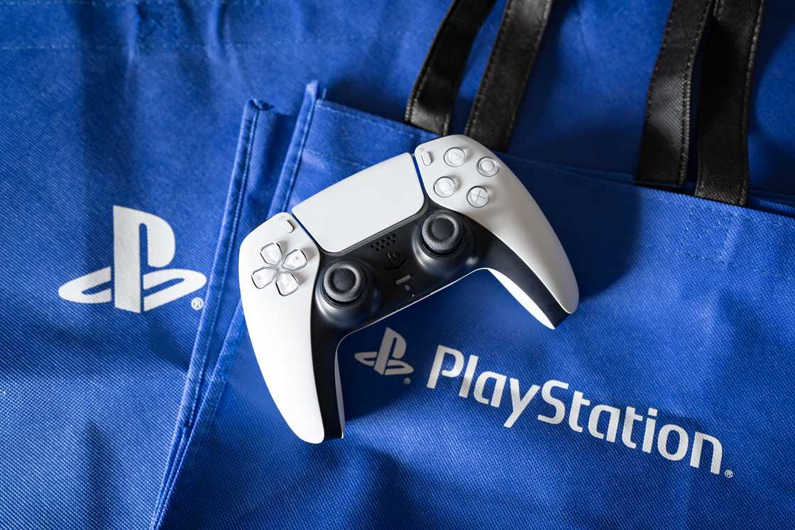 A white PlayStation 5 controller on top of branded bags. A white PlayStation 5 controller on top of branded bags.