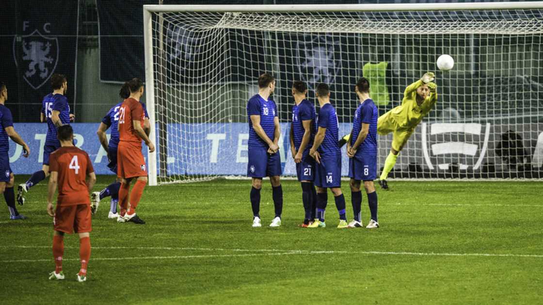 A goalkeeper trying to keep a ball while players watch on in 2018