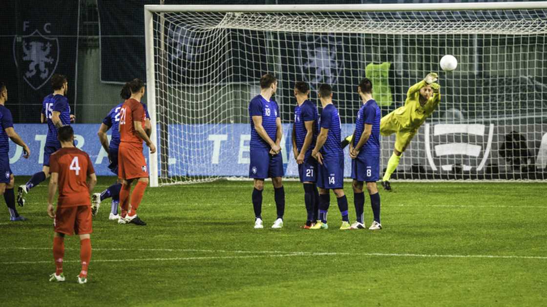 A goalkeeper trying to keep a ball while players watch on in 2018 A goalkeeper trying to keep a ball while players watch on in 2018