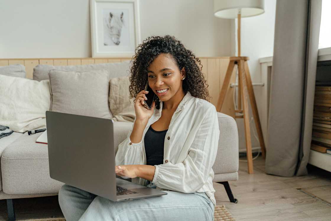 Woman in White Long Sleeve Using a Laptop while Having a Phone Call