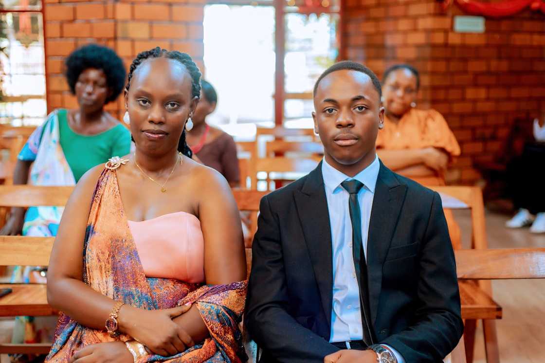 A woman and a young man sit side by side in a formal setting, facing forward. A woman and a young man sit side by side in a formal setting, facing forward.