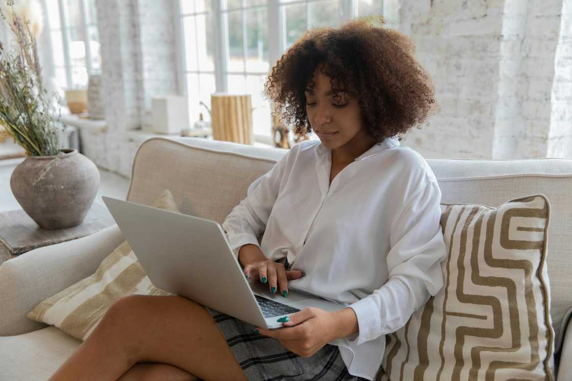 A young woman in a white top and grey and black skirt is using a laptop in a living room