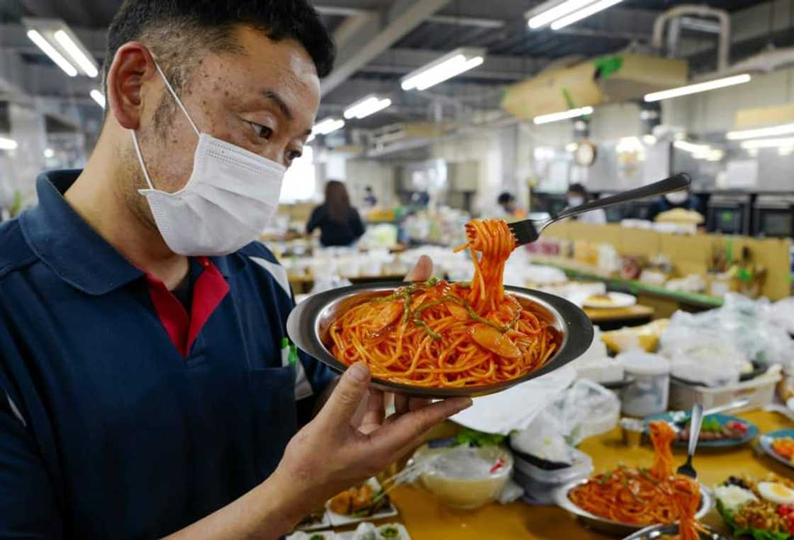 A fork stands suspended in mid-air, strands of 'spaghetti' dangling, as factory head Hiroaki Miyazawa checks a finished plastic food sample