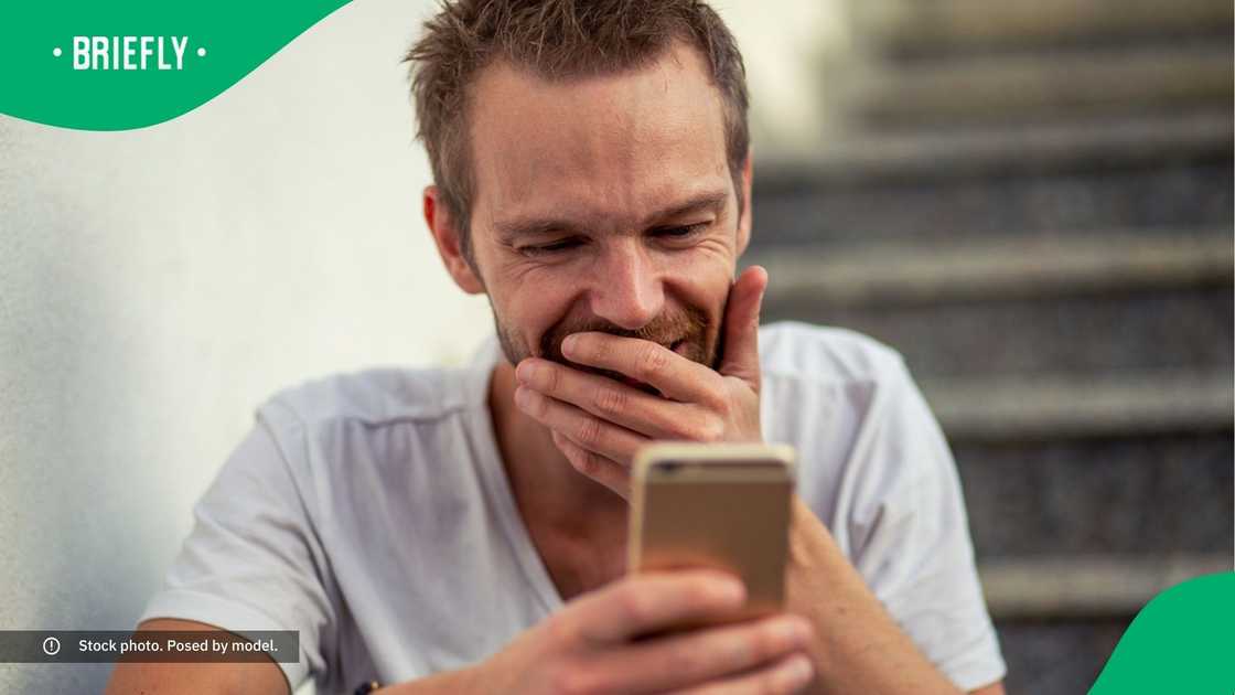 A man covering his mouth with his hand while looking at his phone. A man covering his mouth with his hand while looking at his phone.