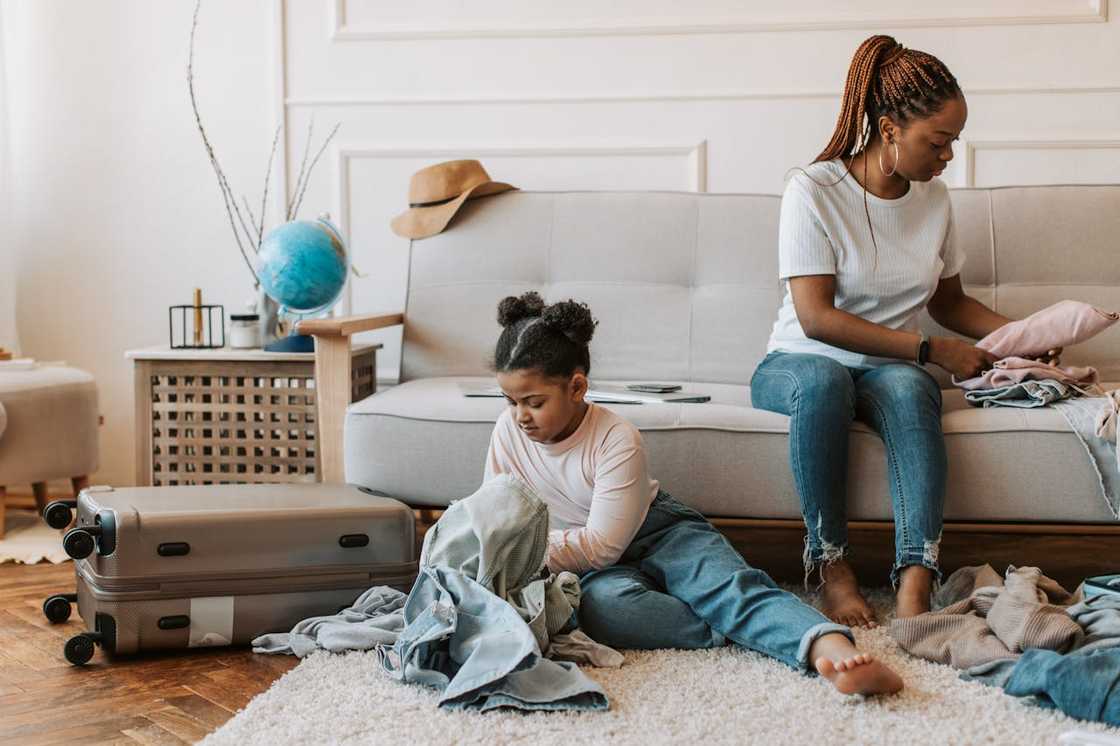 A mother and daughter pack clothes into a suitcase on the living room floor.