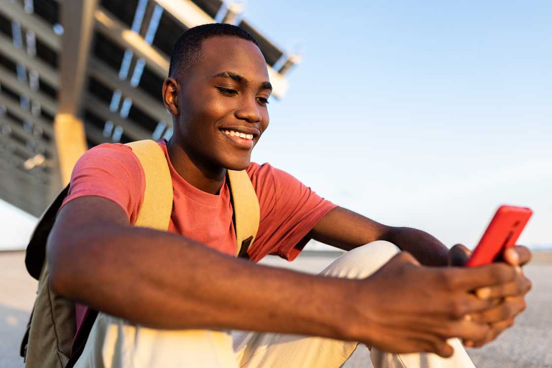 A young man smiling at his phone.