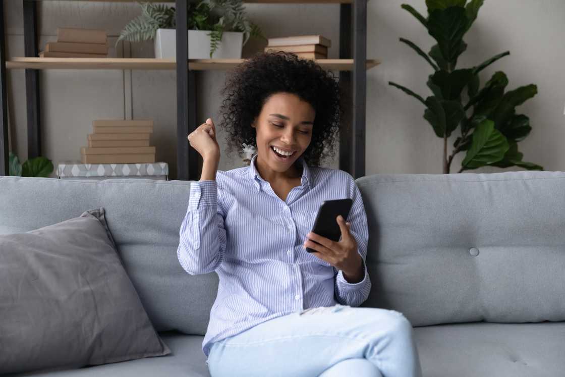 A woman rejoicing while looking at her phone.