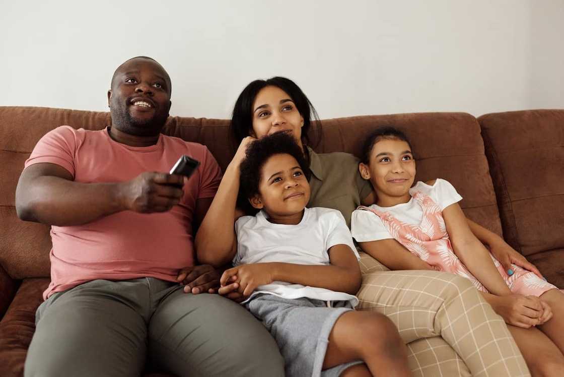 Family sitting on a brown couch watching TV