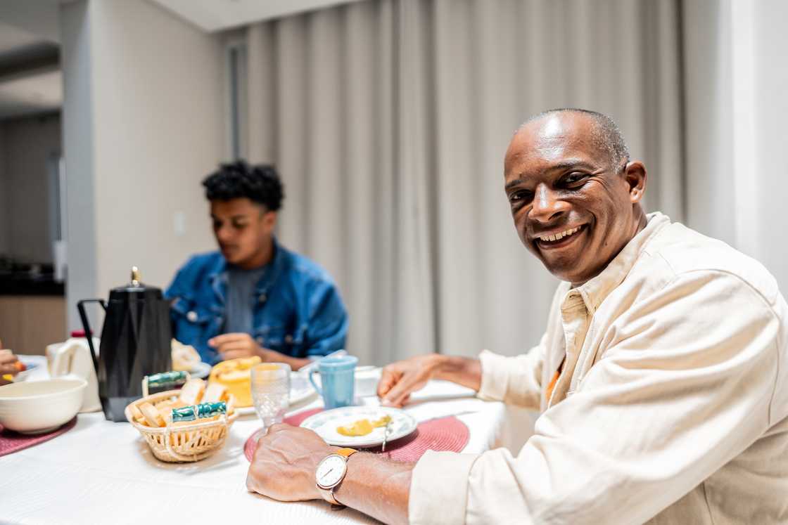 Two people share a meal at a dining table, one smiling at the camera.