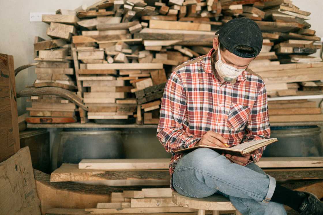 A worker wearing a mask writes notes in a timber workshop.