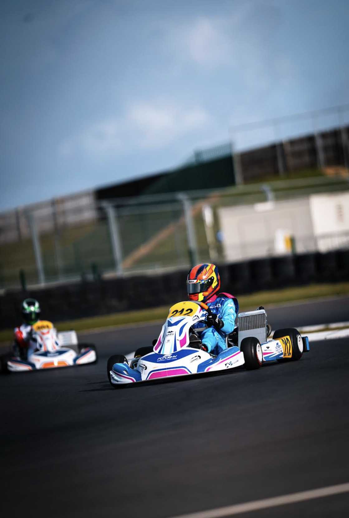 Emma-Rose Dowling races kart number 212 around a circuit corner in a blue racing suit, leading another kart in the background. Emma-Rose Dowling races kart number 212 around a circuit corner in a blue racing suit, leading another kart in the background.