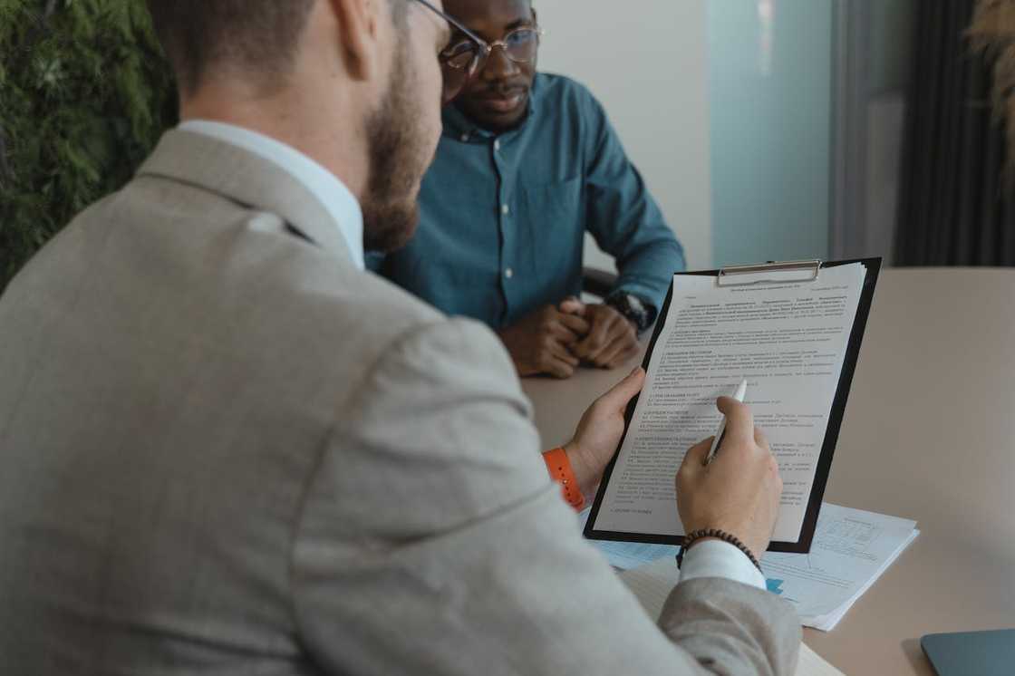 Two men sit at a desk reviewing documents. Two men sit at a desk reviewing documents.