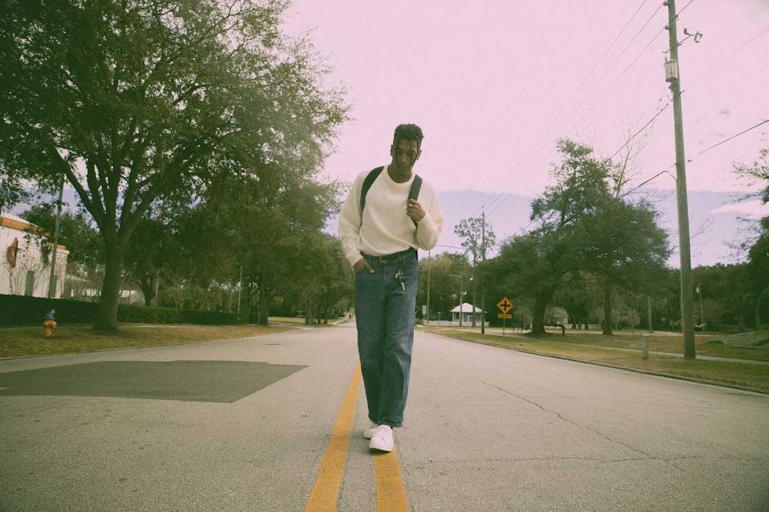 A young man walks alone toward a bus stop in early morning light. A young man walks alone toward a bus stop in early morning light.