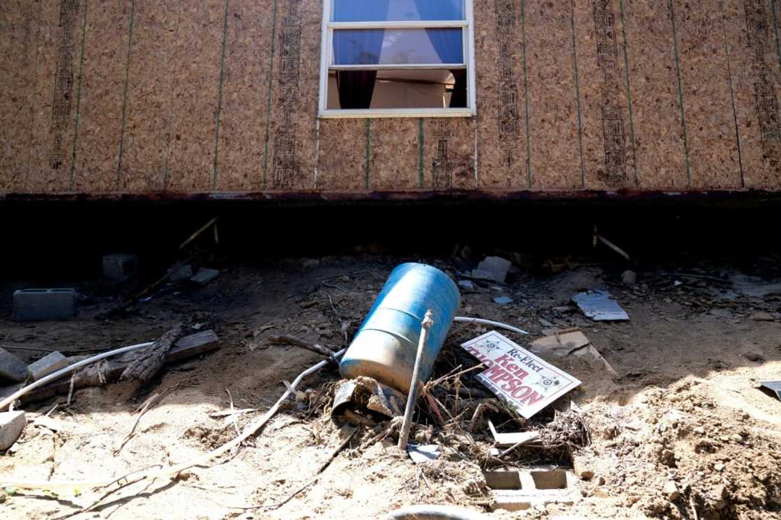 A muddy re-election yard sign in front of a damaged home in Lost Creek