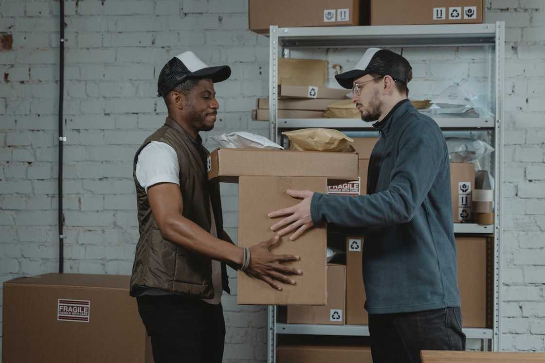 Two workers exchange a cardboard box in a storage room. Two workers exchange a cardboard box in a storage room.