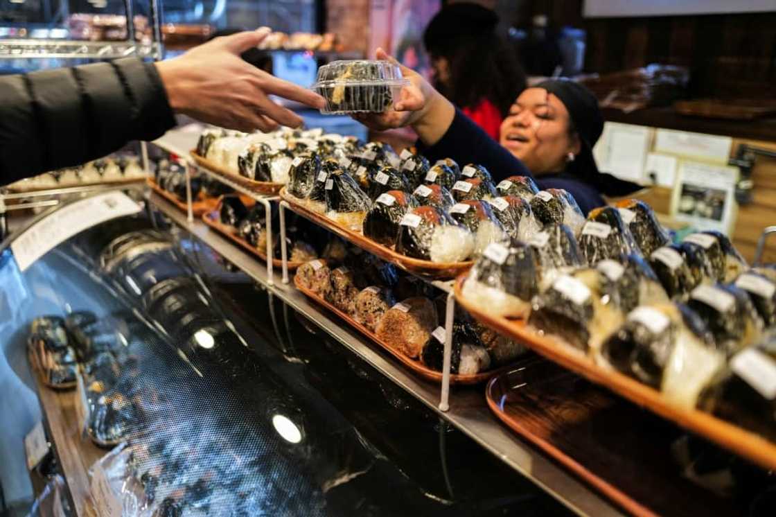 A customer (L) buys a stuffed rice ball, known as "onigiri", at the Omusubi Gonbei shop in Manhattand.