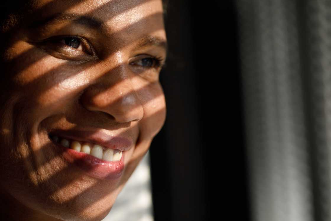 Close-up of a smiling face with striped shadows from window blinds. Close-up of a smiling face with striped shadows from window blinds.