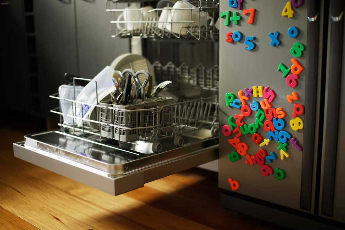 Dishwashing machine with open drawer next to refrigerator covered in childrens' fridge magnets Dishwashing machine with open drawer next to refrigerator covered in childrens' fridge magnets