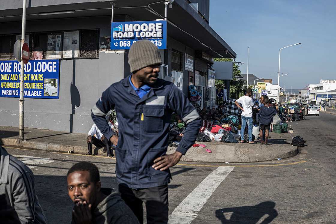 A group of stranded refugees who took refuge while fleeing xenophobic attacks outside the South African Home Affairs offices in Durban stand at a corner near a lodge advertising their rooms, on June 27, 2026