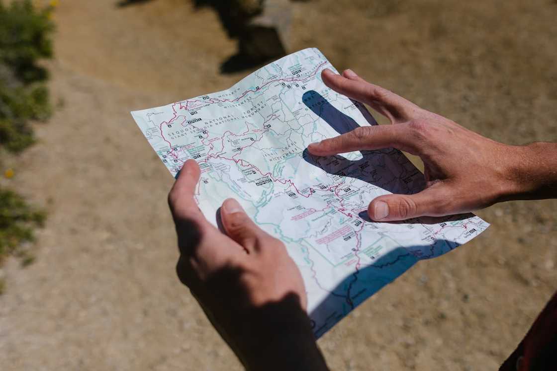 Hands holding a paper map outdoors, pointing to a route on the map.
