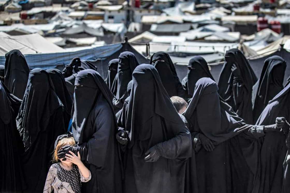 Women and a child queue to receive aid at the Kurdish-run al-Hol camp for relatives of suspected Islamic State group fighters in Syria