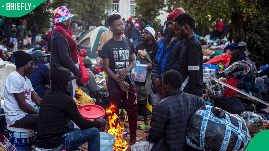 Men stand next to a fire to keep warm as thousands of Malawians take refuge on June 20, 2026 in Sherwood Park outside Durban