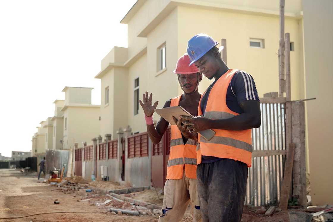 Two construction workers review plans at a housing site. Two construction workers review plans at a housing site.