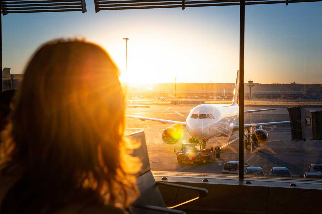 Airport terminal sunrise; calm traveller gazes out window at parked aircraft.