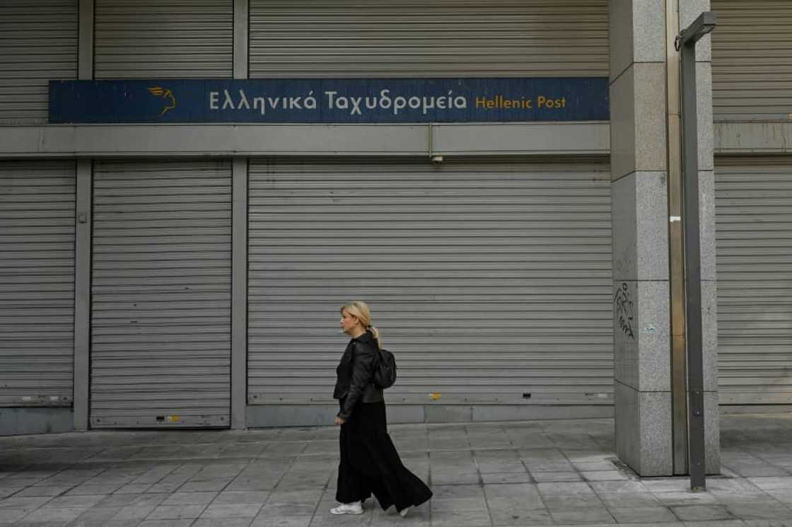 A woman walks past a closed post office during a 24-hour strike in Athens