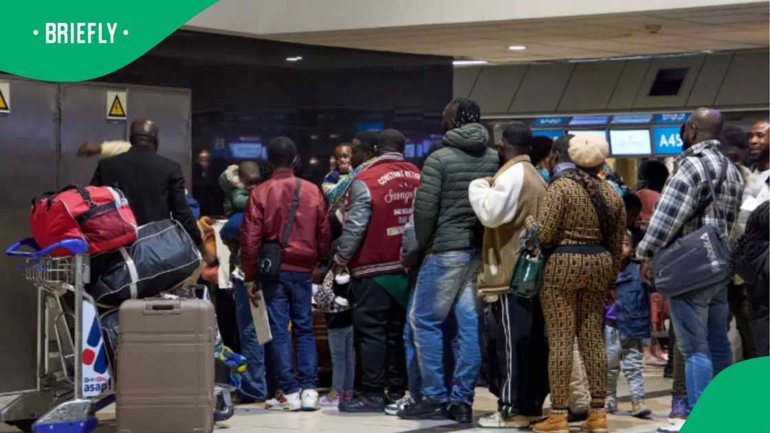 Travelers stood in a long line with suitcases and baggage trolleys as they prepared to board a repatriation flight back to Ghana