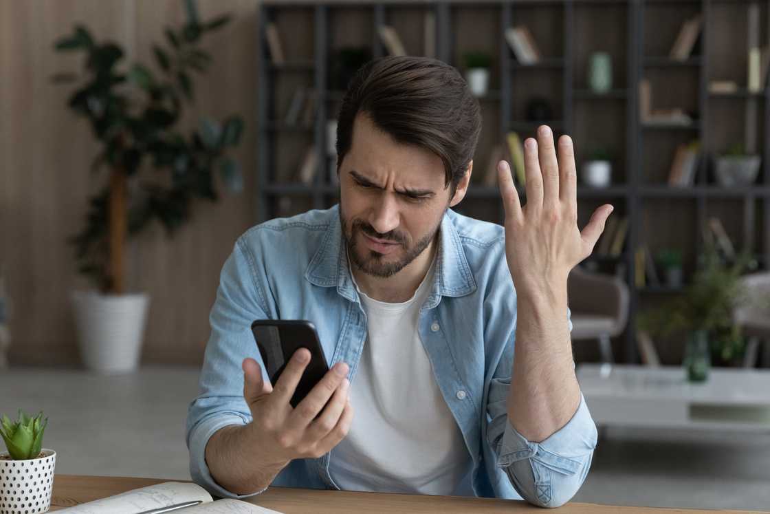 An annoyed man looking at his phone.