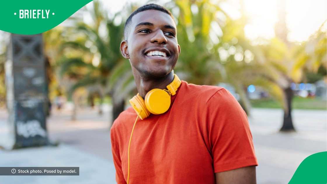 A man posed in a picture wearing an orange top and a yellow headset.