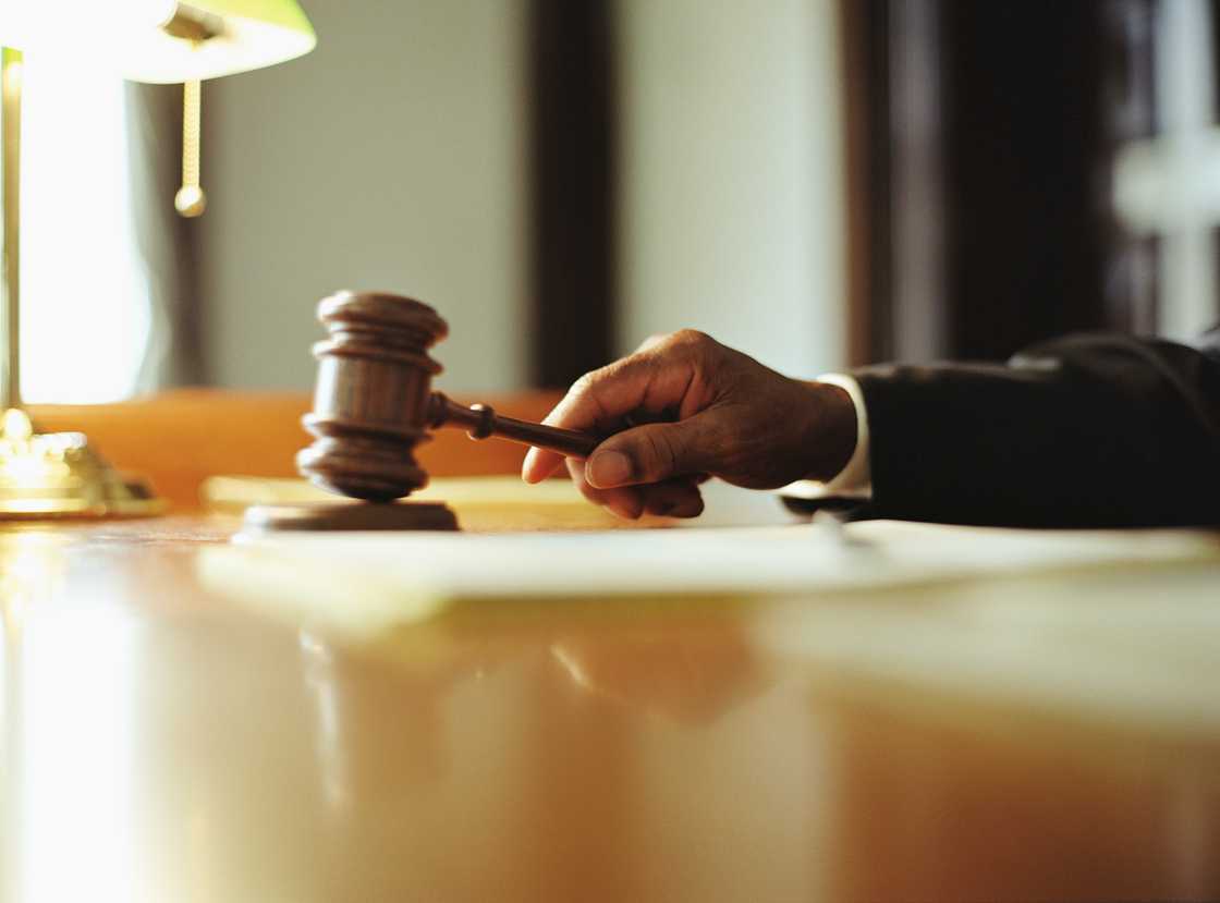 A judge’s hand holding a wooden gavel above a sound block in a formal courtroom.
