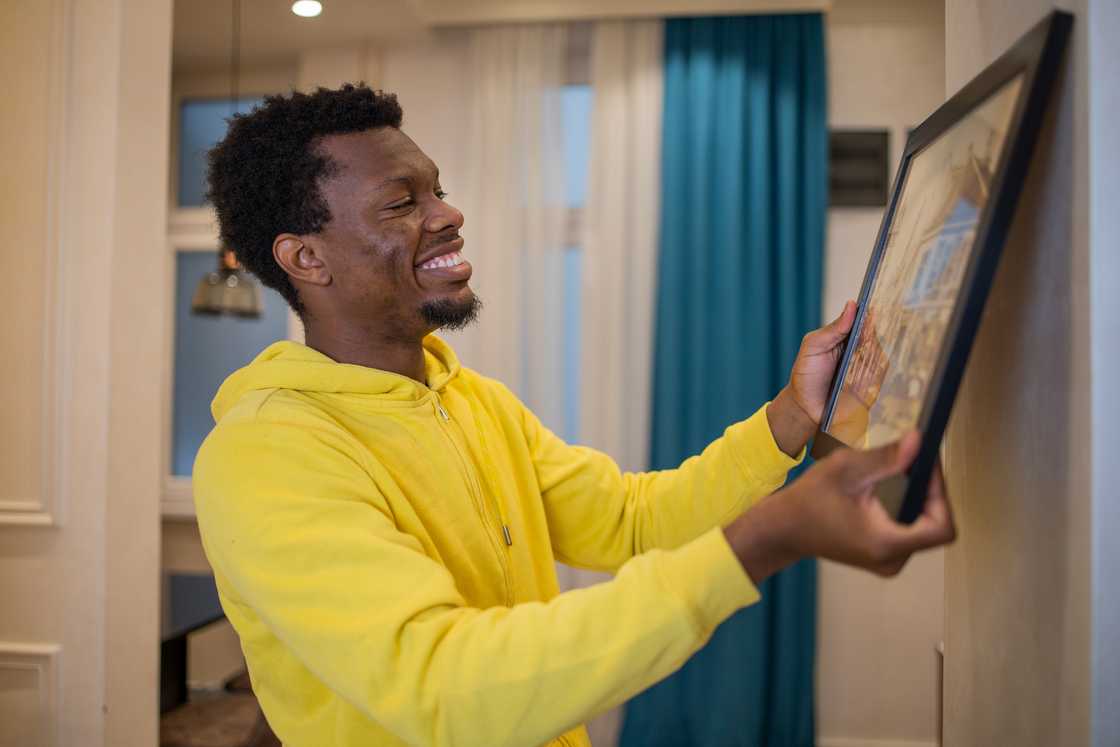 Man replacing family photos with framed Bible verses on a hallway wall.